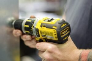 Gros plan d'une main tenant une perceuse-visseuse DeWalt 18V jaune et noire en atelier