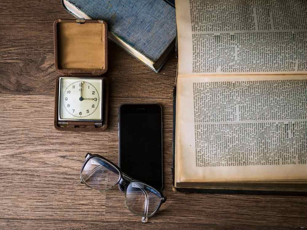 livre ouvert, montre, smartphone, lunettes et boîte sur table en bois
