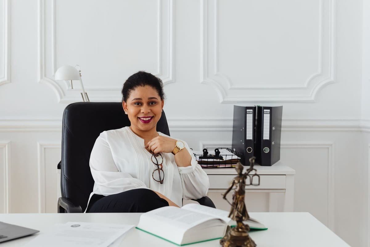 Femme souriante dans un bureau, devant un bureau avec livre et statue Femme souriante dans un bureau, devant un bureau avec livre et statue