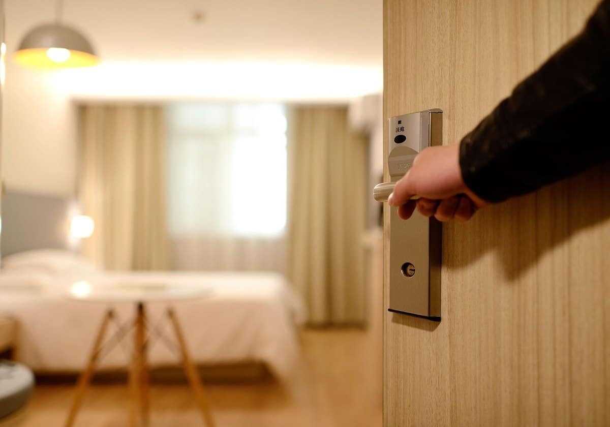 Une main ouvre la porte d'une chambre avec lit et lampe Une main ouvre la porte d'une chambre avec lit et lampe