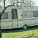 Caravane beige posée sur pelouse arbre à feuilles ciel bleu