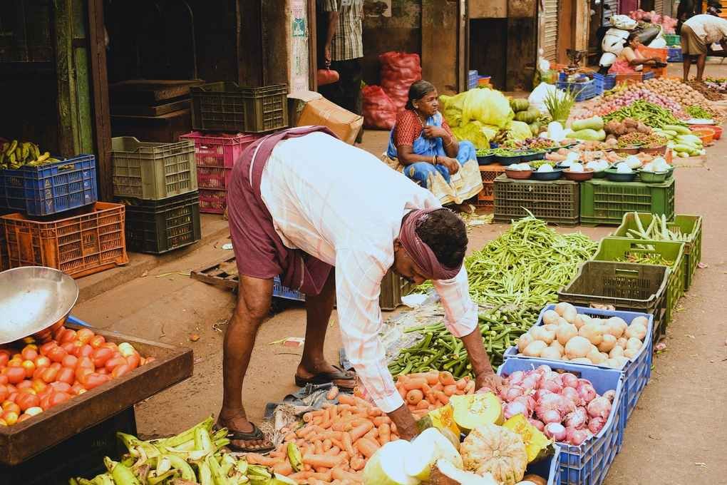 Homme choisissant des légumes sur un marché, étals colorés, autres clients présents Homme choisissant des légumes sur un marché, étals colorés, autres clients présents