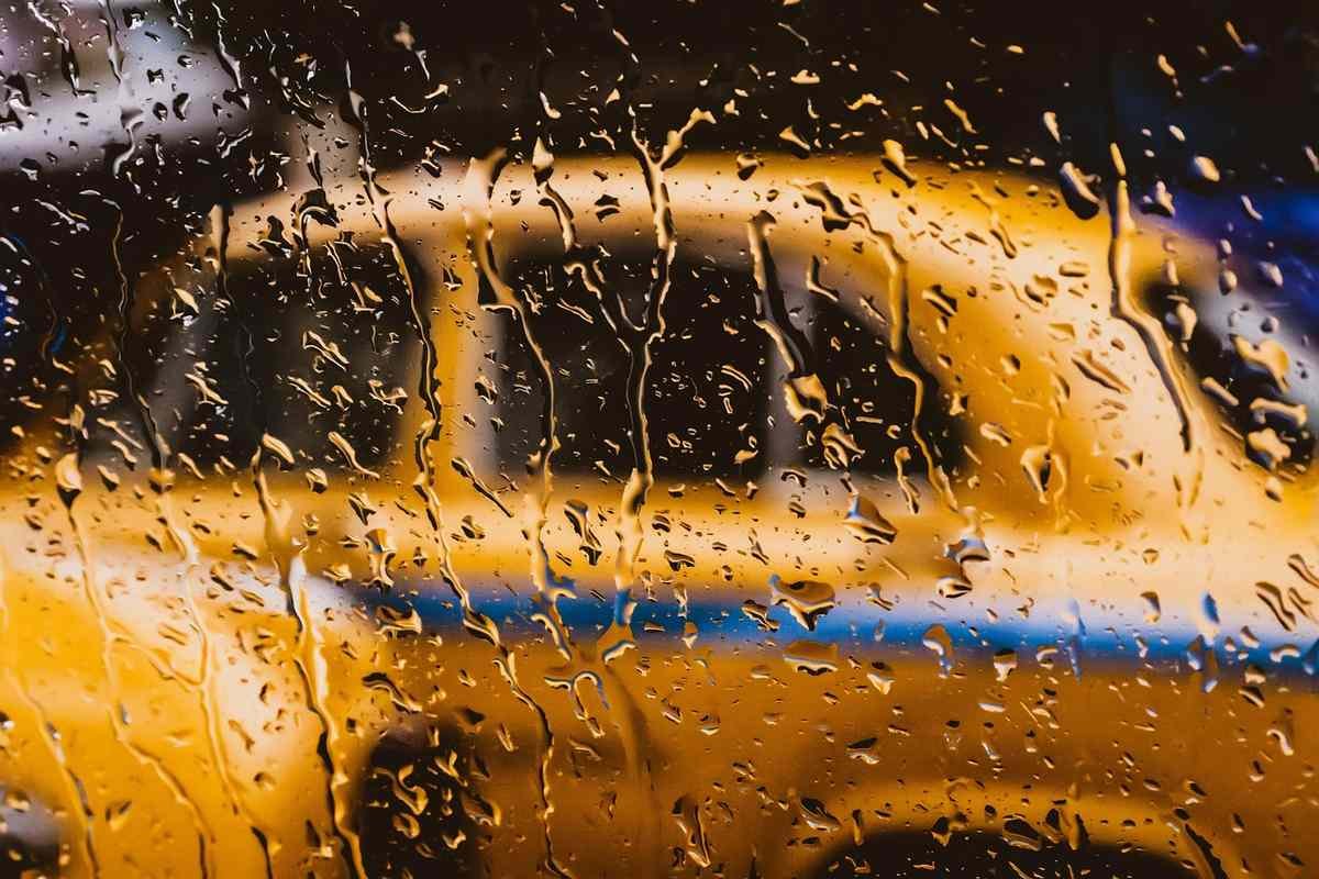 Vitre mouillée masquant un taxi jaune en mouvement sous la pluie