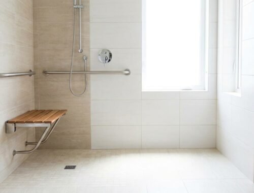 Salle de bain accessible senior, douche de plain-pied avec barre d'appui et siège, carrelage clair, lumineuse