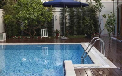 Une piscine extérieure avec terrasse en bois, parasol bleu et végétation