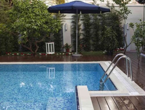 Une piscine extérieure avec terrasse en bois, parasol bleu et végétation