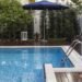 Une piscine extérieure avec terrasse en bois, parasol bleu et végétation